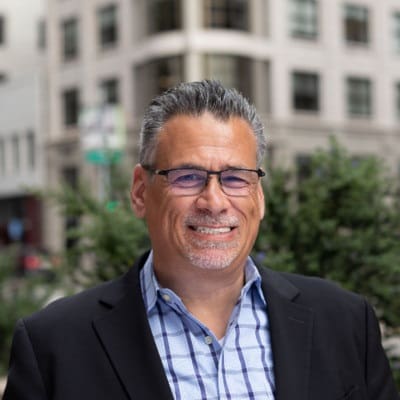 A man with glasses smiling in front of a building offering Technical Recruiting Services in the San Francisco Bay Area.