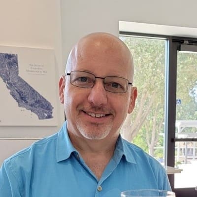 A bald man in the San Francisco Bay Area smiles while holding a glass of wine.