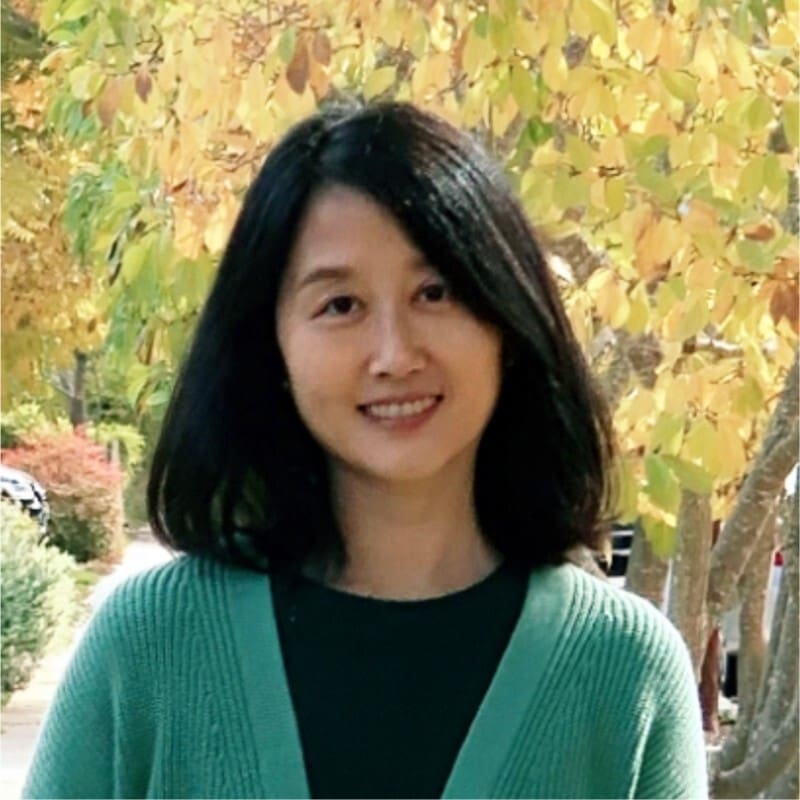 A woman in a green cardigan smiles in front of a tree in the San Francisco Bay Area.