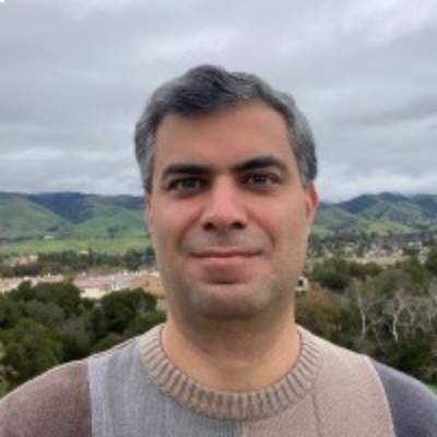 A man in a sweater standing in front of a mountain, offering technical recruiting services.