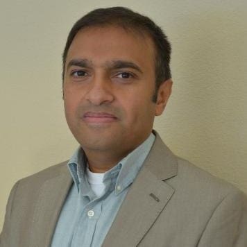 A man in a tan suit standing in front of a wall in the San Francisco Bay Area.