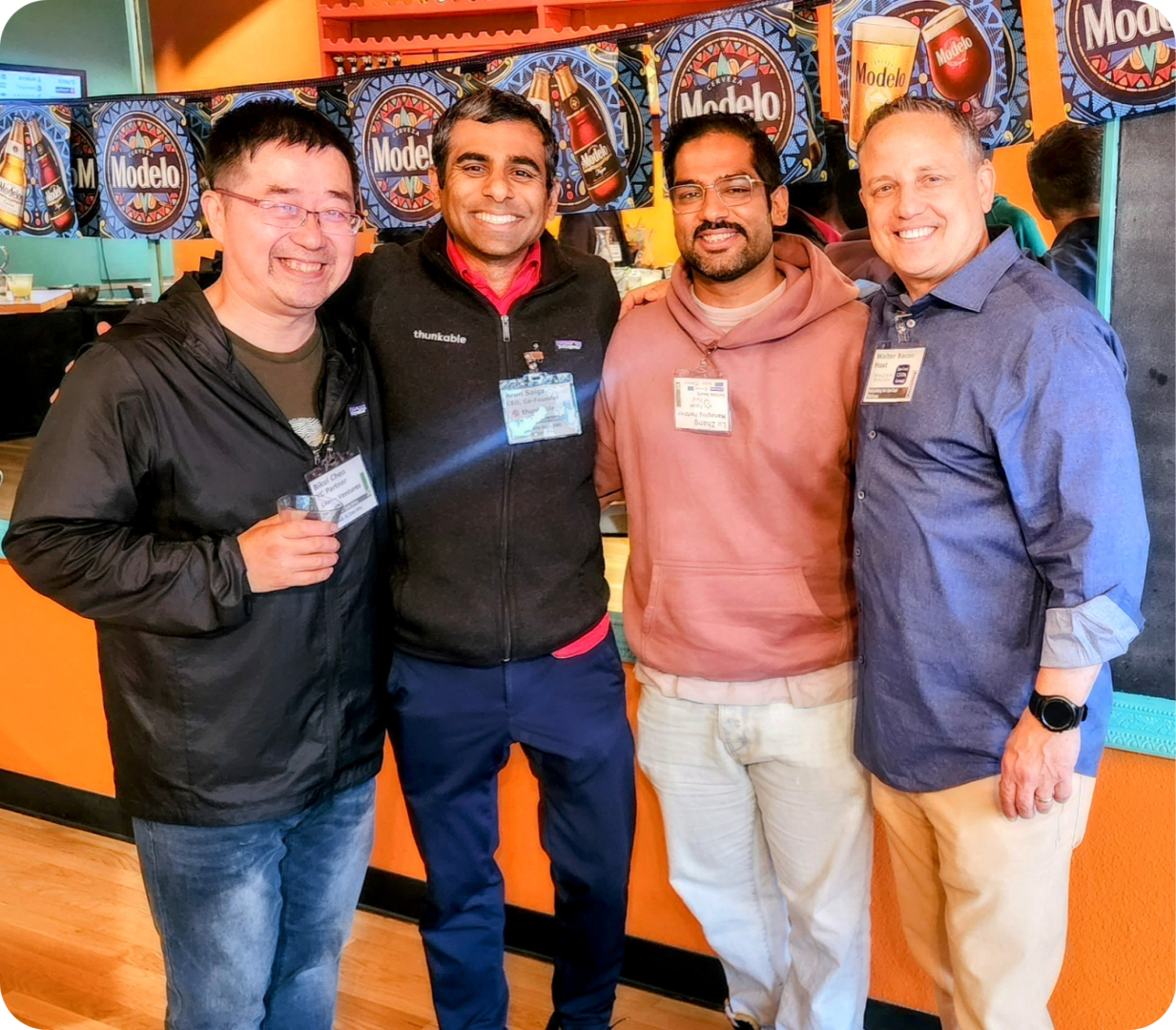 Four men smiling with Modelo beer signs.