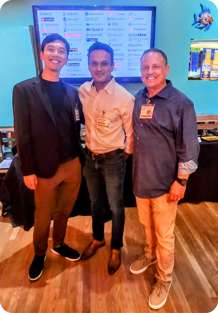 Three men stand together smiling in a conference room.