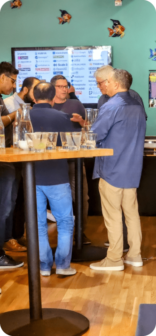 Men gather around a table with drinks.
